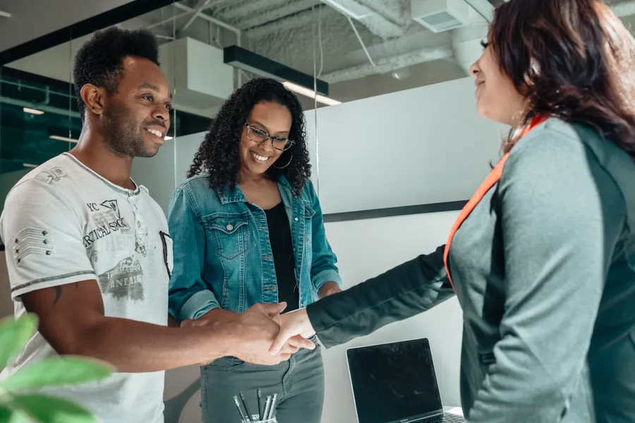 Stock photo of three adults in an office meeting, with a handshake across a desk